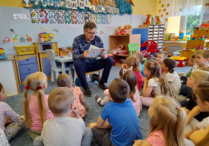 Dzieci siedzą na dywanie słuchają opowiadania czytanego przez Burmistrza Aleksandrowa Łódzkiego Jacka Lipińskiego.